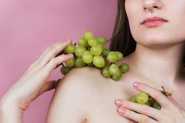 Faceless portrait of a  woman with septum holding grapes  on her shoulder and chest