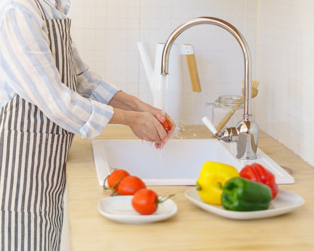 Faceless senior woman in apron preparing vegetables for salad while cooking in modern kitchen at