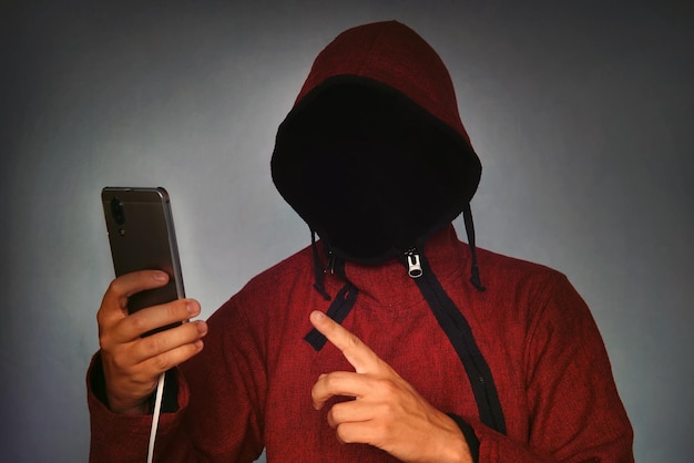 Persona incappucciata irriconoscibile senza volto che utilizza il furto di identità del telefono cellulare e il concetto di crimine tecnologico focus selettivo sull'hacking del corpo un furto di identità dello smartphone