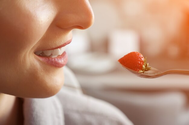 Faceless woman eating strawberry and smiling, sunlight