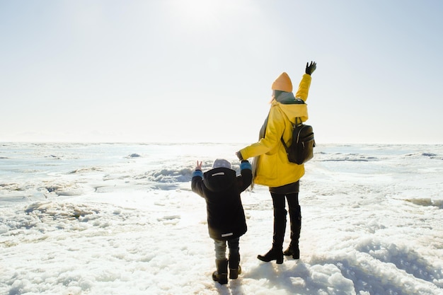 写真 黄色いレインコートを着た顔の見えない女性と子供が立って凍った海を見ている