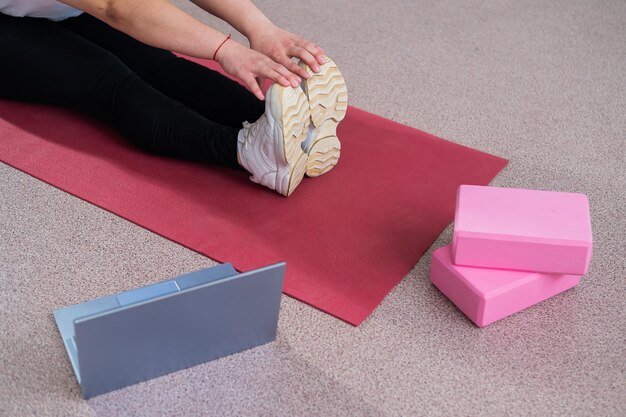 A faceless woman is watching an online yoga lesson on a laptop distance sports training