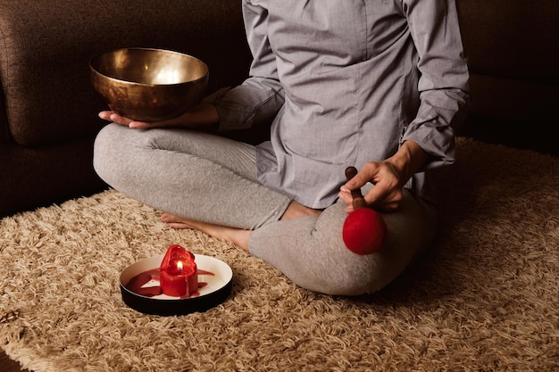 Photo faceless woman meditates at home on carpet and plays on copper singing bowl. sound therapy, recreation, meditation.