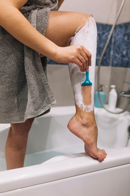 Faceless woman shaving legs