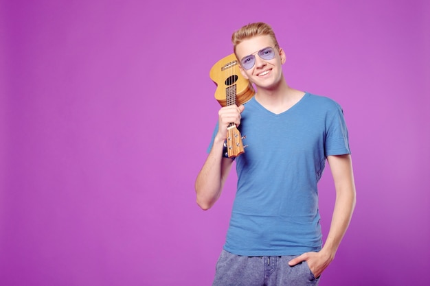 Fachion beauty funny man with ukulele in hands on purple background copyspace