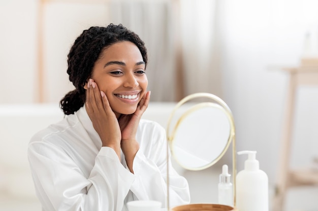 Facial Care Attractive Black Woman Looking At MirrorAnd Touching Face