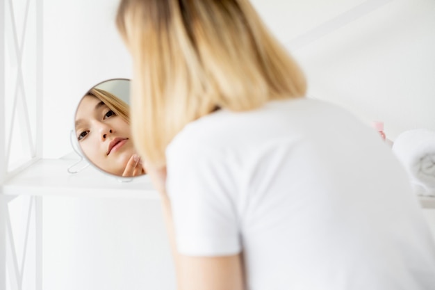 Cura del viso trattamento della pelle routine mattutina attraente giovane donna con un viso perfettamente pulito nel riflesso speculare su sfondo chiaro