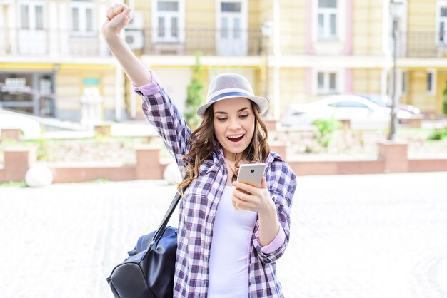 Emozione facciale che esprime il concetto di buona notizia di internet in roaming di connessione chat. ritratto di una bella signora allegra e gioiosa che alza le mani guardando il telefono in mano che riceve l'invio di sms