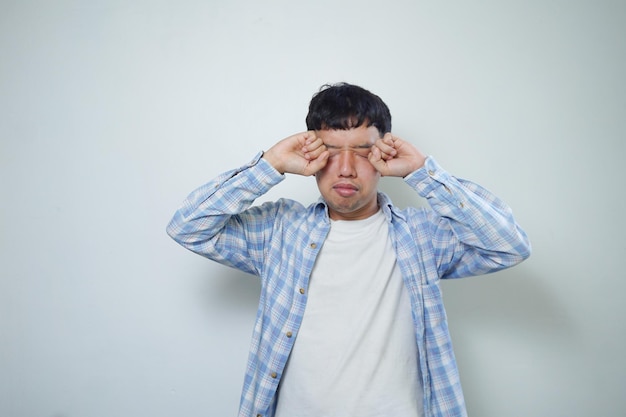 Facial expression of a sleepy asian man rubbing his eyes isolated on a white background