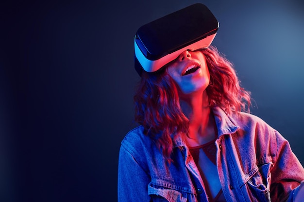 Facial expression of young girl with virtual reality glasses on head in red and blue neon in studio