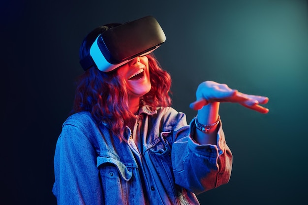 Facial expression of young girl with virtual reality glasses on head in red and blue neon in studio