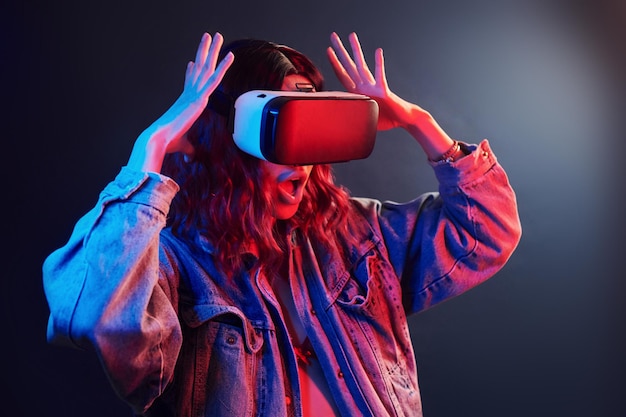 Facial expression of young girl with virtual reality glasses on head in red and blue neon in studio