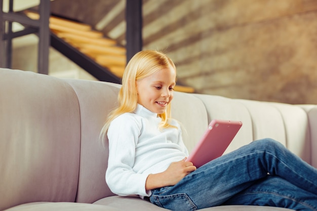 Facial expressions. Joyful preschooler sitting on sofa while playing online game