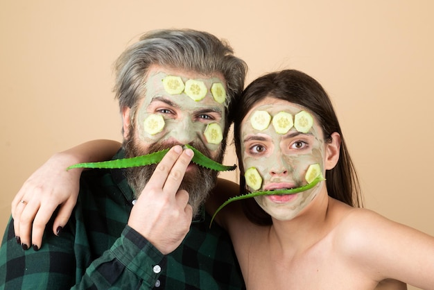 Facial mask for fun couple. Funny couple getting facial care with aloe vera. Beautician is making facial mask on man and woman face. Cosmetologist making facial procedure with aloe vera and cucumber.