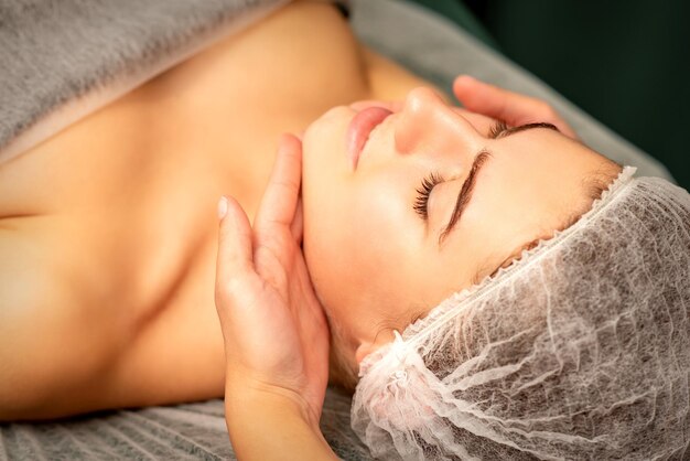 Facial massage Hands of a masseur massaging neck of a young caucasian woman in a spa salon the concept of health massage