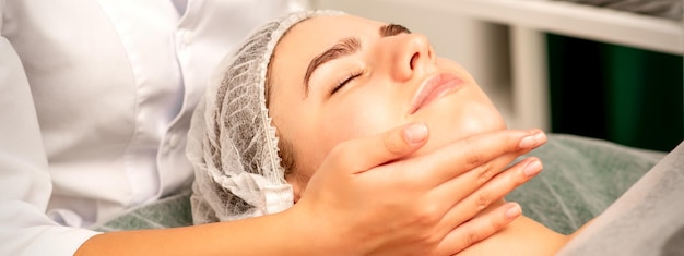 Массаж лица руки массажиста, массирующего шею молодой кавказской женщины в спа-салоне концепция оздоровительного массажа