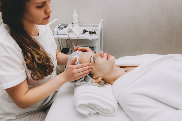 Facial massage is prepared in the spa Doctors hands Treatment for healthy skin Head of a young woman Cleansing rejuvenation Dermatological face mask Detox therapy