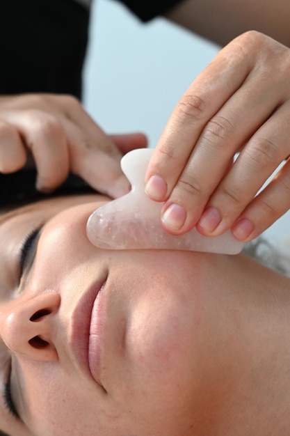 Massaggio facciale vista laterale donna europea che riceve un massaggio facciale con un raschietto a gouache nel salone termale primo piano