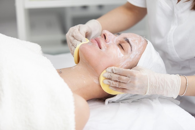 Facial massage and skincare treatment Dermatologist hands cleaning relaxed serene young woman face with pads in beauty salon during skincare treatment Face massage