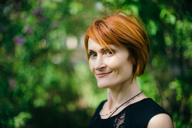 Facial portrait of amazing smiling woman with red hair in black dress with copy space on green