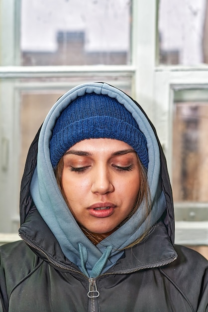 Facial portrait of a pretty girl in a hat and dark jacket with a hood