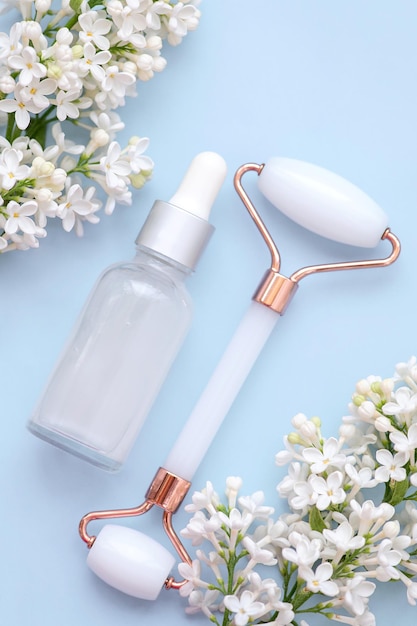 Facial roller serum and white lilac flowers on a blue background View from above