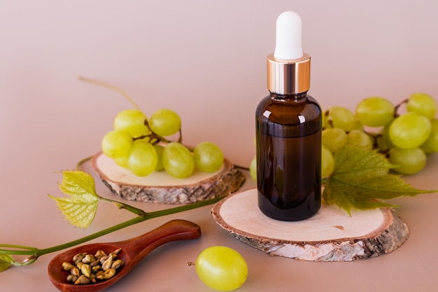 Siero facciale o olio cosmetico di semi d'uva in una bottiglia con una pipetta si erge su un pezzo di legno e bacche di uva matura il concetto di bellezza