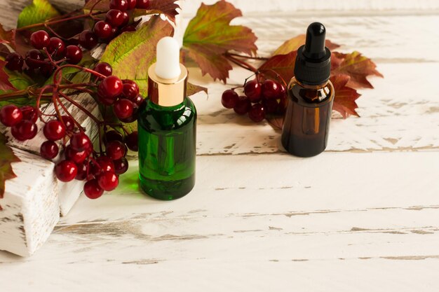 Facial serum in glass bottles with a pipette, viburnum leaves and berries on a white wooden background.