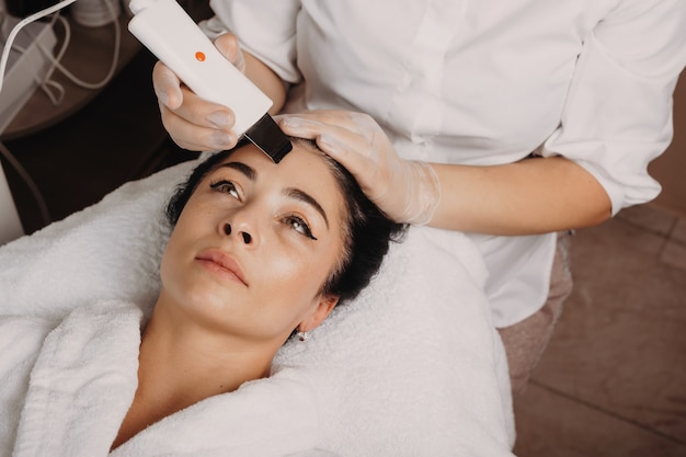 Facial skin care procedure done at the salon with modern apparatus by a young spa worker