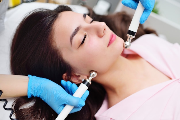 Facial skin rejuvenation by microcurrent therapy in a modern cosmetology clinic. A cosmetologist uses a special device to perform a facial rejuvenation procedure for a pretty young girl.