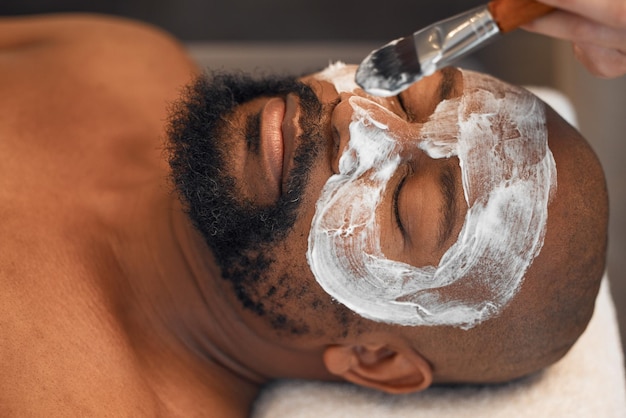 Facial skincare and relax with black man in spa for beauty luxury and mud mask Wellness therapy and health with male and beautician brush cosmetics product on face for peace massage and salon