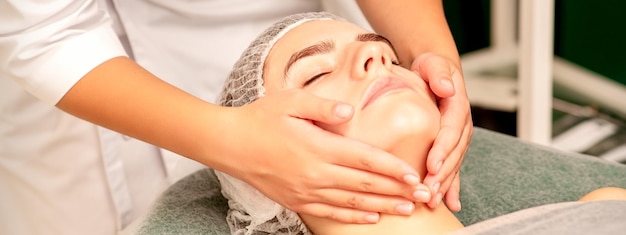 Facial treatment massage Beautiful young caucasian woman with perfect skin receiving face and neck massage at a beauty spa