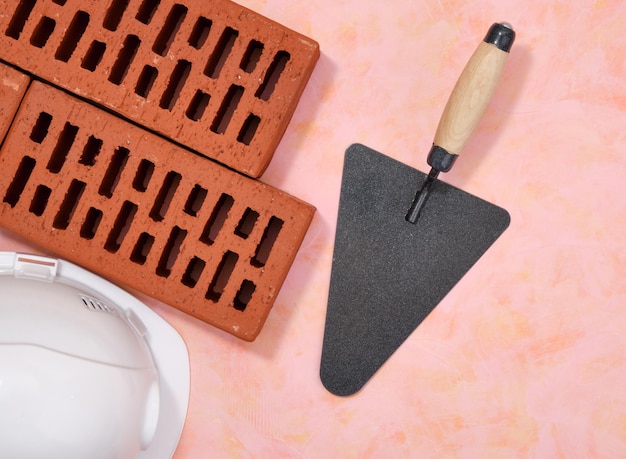 Photo facing bricks metal trowel with wooden handle and helmet flat lay