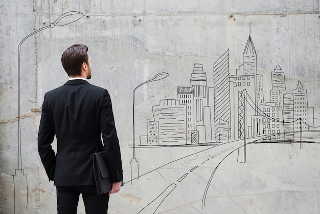 Facing a wall. Rear view of young man holding briefcase while standing outdoors and against the concrete wall