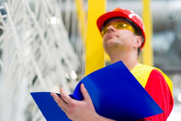 Foto ingegnere di fabbrica che controlla la linea di produzione con una cartella blu con i documenti