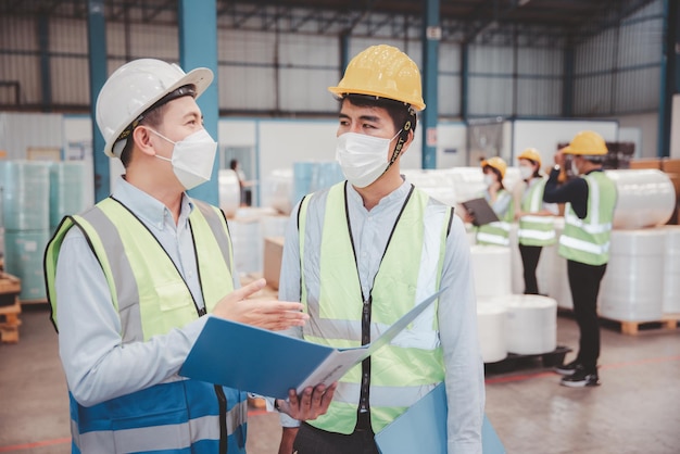 Factory manager and engineer in  medical mask and safety protective suite using computer laptop and digital tablet working discuss together