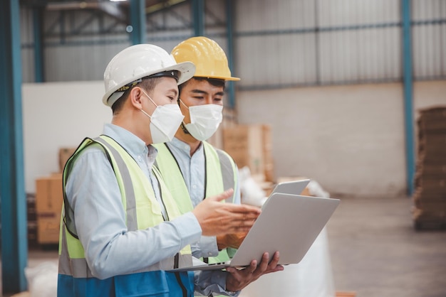 Factory manager and engineer in  medical mask and safety protective suite using computer laptop and digital tablet working discuss together