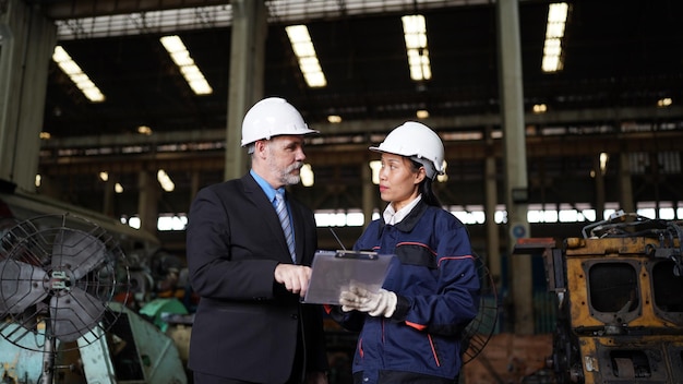 Factory manager and female engineer in factory and inspecting\
factory in industry plant background