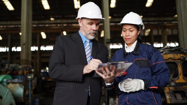 Factory manager and female engineer in factory and inspecting\
factory in industry plant background