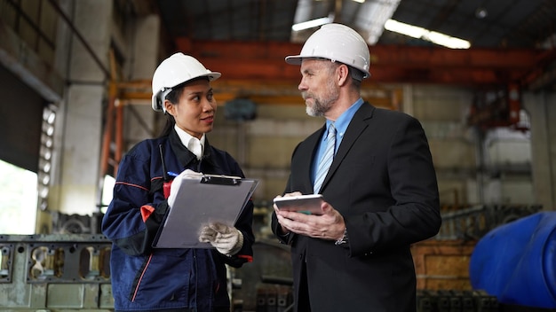 Factory manager and female engineer in factory and inspecting\
factory in industry plant background