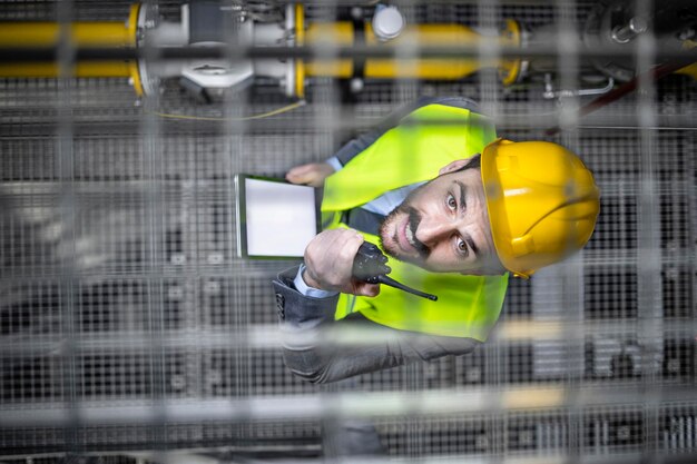 Photo factory manager in reflective vest and protective equipment holding tablet and looking to the camera