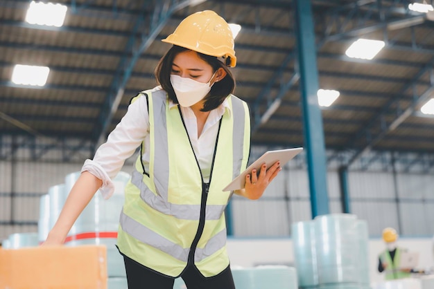 Foto personale donna di fabbrica in maschera medica e sicurezza protettiva utilizzando tablet digitale che lavora controllando lo stoccaggio dell'inventario nel magazzino tessile