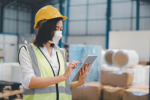 Foto personale donna di fabbrica in maschera medica e sicurezza protettiva utilizzando tablet digitale che lavora controllando lo stoccaggio dell'inventario nel magazzino tessile