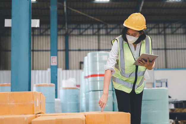 Factory woman staff in medical face mask and protective safety using digital tablet working checking inventory storage at textile warehouse