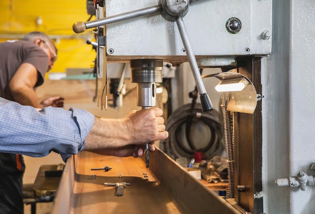 factory worker installs the drill into the machine to drill holes in metal beams