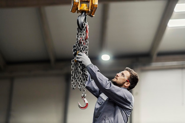 A factory worker putting chains on an industrial hook in a metalwork factory