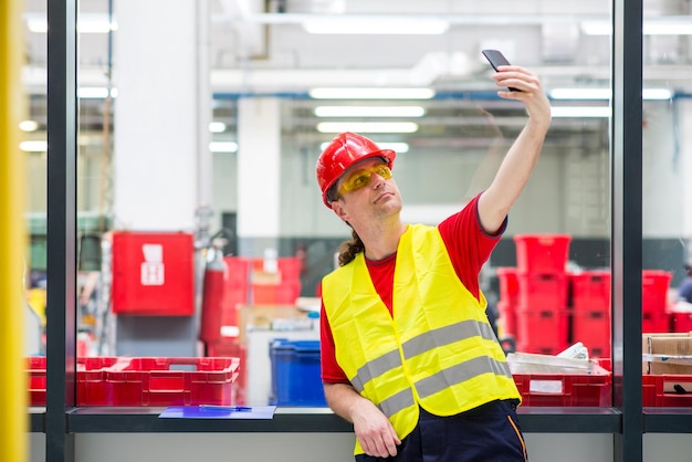写真 工場内で携帯電話でセルフィーを撮っている工場労働者