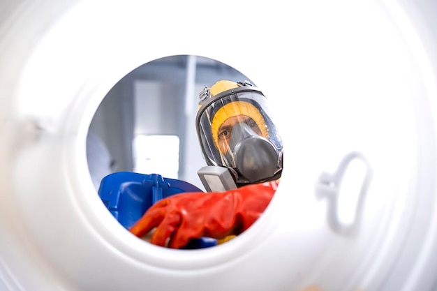 Factory worker with gas mask and gloves pouring chemicals into the barrel