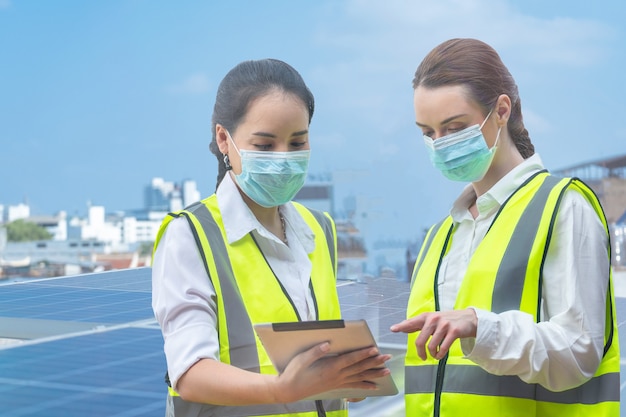 factory worker women with face mask meeting to inspect at rooftop of solar cell panel