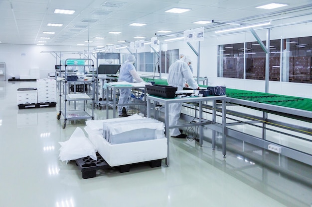 Factory workers in white lab suits producing tv sets on a green assebly line with some modern equipment